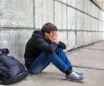 Sad Young Man sit by the Wall on the Street